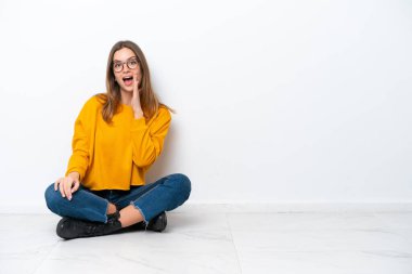 Beyaz arka planda izole bir şekilde yerde oturmuş ağzı açık bağıran beyaz bir kadın.
