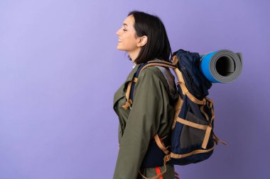 Arka planda büyük bir sırt çantası olan genç dağcı kadın yan pozisyonda gülüyor.