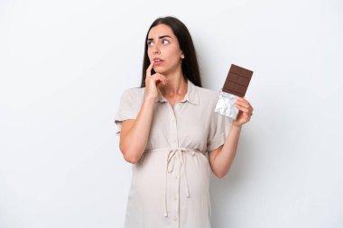 Beyaz arka planda izole edilmiş beyaz bir kadın hamile ve elinde çikolata tutarken şüpheleri var.
