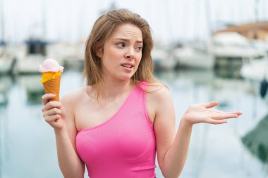 Açık havada kornet dondurmalı genç kızıl saçlı kadın. Suratı şaşırmış.