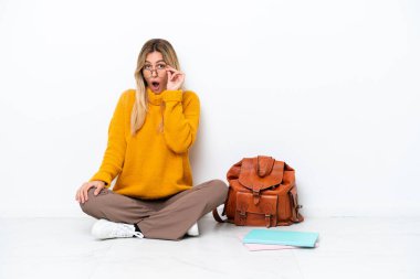 Bir katta oturan Uruguaylı öğrenci kadın beyaz arka planda gözlüklü ve şaşırmış.