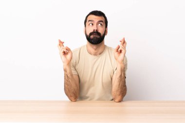 Masada sakallı beyaz bir adam parmaklarını çapraz yapıp en iyisini diliyor..