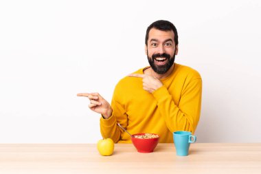 Masada kahvaltı yapan beyaz bir adam şaşırmış ve işaret ediyor..