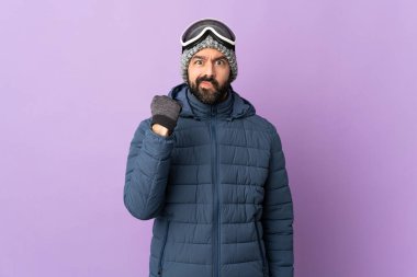 Kar kaykayı gözlüklü kayakçı mutsuz bir ifadeyle mor arka planda.