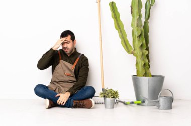 Bahçıvan adam baş ağrısıyla yerde oturuyor.