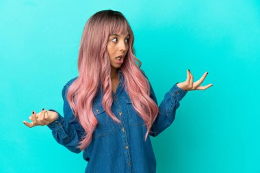 Mavi arka planda pembe saçlı melez bir kadın. Sürpriz bir ifadeyle yan tarafa bakıyor.