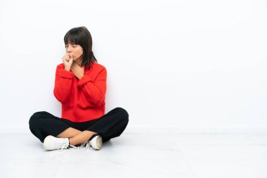 Beyaz arka planda soyutlanmış bir şekilde yerde oturan genç melez kadın öksürükten muzdarip ve kötü hissediyor.