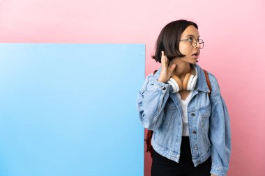 İzole edilmiş arka planda büyük bir pankartıyla melez genç bir kız öğrenci elini kulağına koyarak bir şeyler dinliyor.