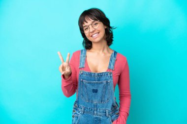 Önlüklü, izole edilmiş, gülümseyen ve zafer işareti gösteren genç bir kadın.