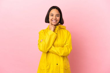 Yağmura dayanıklı bir ceket giyen, izole edilmiş arka planda mutlu ve hoş bir ifadeyle gülümseyen genç Latin bir kadın.