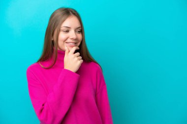 Genç Litvanyalı bir kadın mavi arka planda izole edilmiş, yana bakıyor ve gülümsüyor.