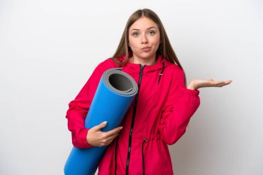 Genç bir kadın yoga derslerine giderken beyaz arka planda bir minder tutuyor.   