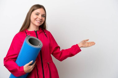 Genç bir kadın yoga derslerine giderken beyaz arka planda bir minder tutuyor.   