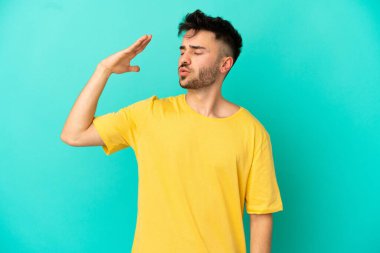 Kafkasyalı genç adam mavi arka planda izole edilmiş, yorgun ve hasta bir ifadeyle.