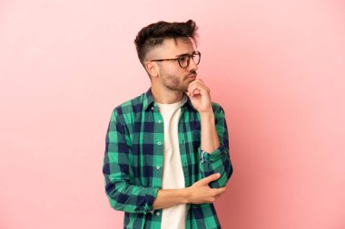 Pembe arka planda soyutlanmış genç beyaz bir adamın şüpheleri ve düşünceleri var.