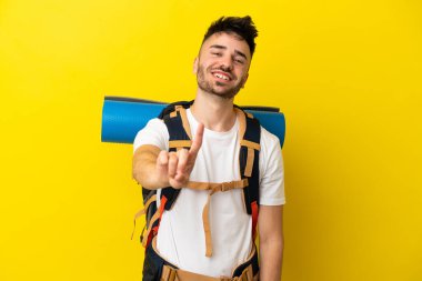 Sarı arka planda izole edilmiş büyük sırt çantalı genç beyaz adam parmağını kaldırıyor ve gösteriyor.