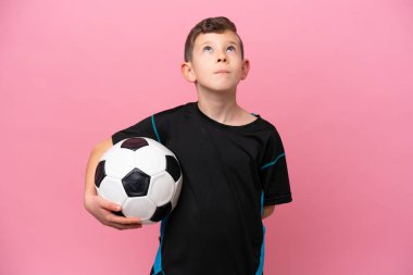 Küçük beyaz futbolcu çocuk pembe arka planda izole edilmiş ve yukarı bakıyor.
