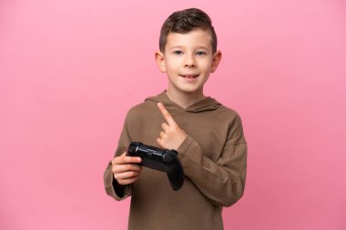 Pembe arka planda izole edilmiş bir bilgisayar oyunu kontrolörüyle oynayan beyaz çocuk bir ürünü sunmak için kenarı işaret ediyor.