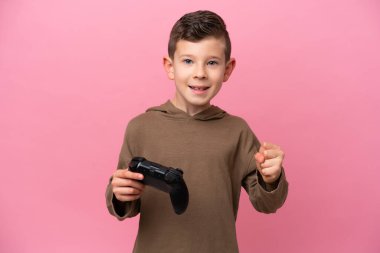Pembe arka planda izole edilmiş bir bilgisayar oyunu kontrolörüyle oynayan küçük beyaz çocuk galibiyeti kutluyor.