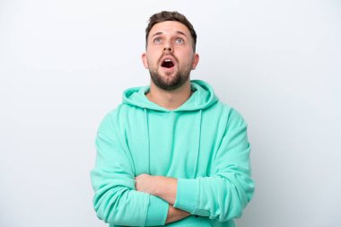 Beyaz arka planda izole edilmiş genç beyaz adam yukarı bakıyor ve şaşırmış bir ifadeyle