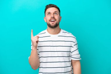 Mavi arka planda izole edilmiş genç beyaz adam yukarı bakıyor ve şaşırıyor.
