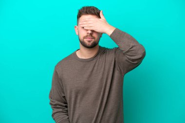 Genç beyaz adam mavi arka planda tek başına, gözleri elle kapatıyor. Bir şey görmek istemiyorum.