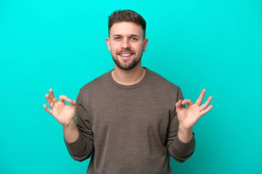Mavi arka planda izole edilmiş beyaz bir adam iki eliyle tamam işareti gösteriyor.