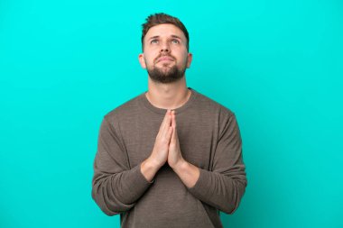 Mavi arka planda izole edilmiş genç beyaz adam avuç içlerini bir arada tutuyor. İnsan bir şey ister.