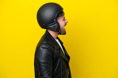 Sarı arka planda izole edilmiş motosiklet kasklı beyaz bir adam yan pozisyonda gülüyor.