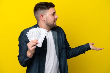 Kafkas 'lı genç bir adam, sarı arka planda bir sürü para alıyor. Sürpriz bir ifadeyle yan yana bakarken...