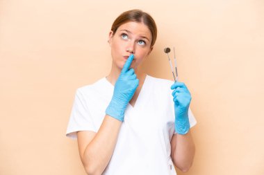 Beyaz dişçi kadının elinde bej arka planda izole edilmiş aletler var.