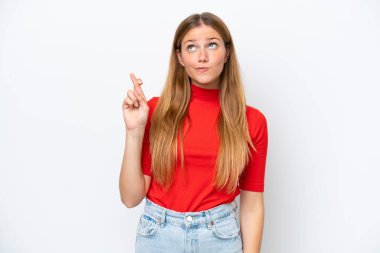 Beyaz arka planda izole edilmiş beyaz tenli genç bir kadın parmaklarını çapraz yapıp en iyisini diliyor.