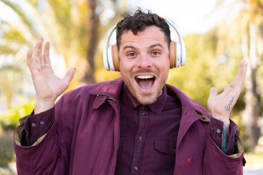 Açık havada genç beyaz bir adam şaşırdı ve müzik dinliyor.