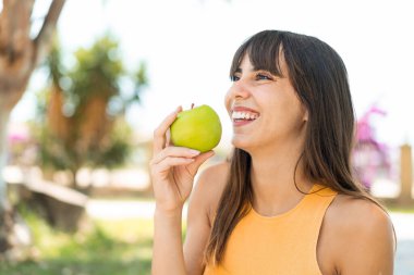 Açık havada elinde mutlu bir ifadeyle elma tutan genç bir kadın.