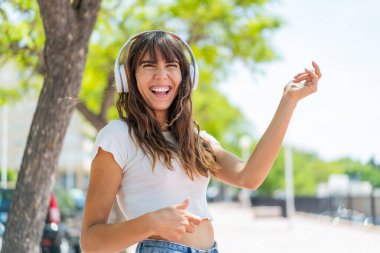 Açık havada müzik dinleyen ve gitar hareketi yapan genç bir kadın.