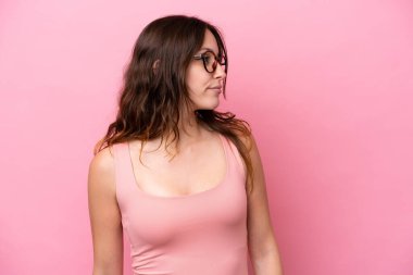 Pembe arka planda izole edilmiş genç beyaz kadın yan tarafa bakıyor.