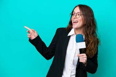 Genç TV sunucusu, mavi arka planda izole edilmiş, parmağını yana doğru gösteren ve bir ürün sunan bir kadın.