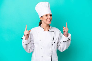 Kafkasyalı genç aşçı kadın mavi arka planda izole edilmiş. Harika bir fikre işaret ediyor.