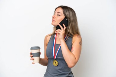 Young Rumanian woman with medals isolated on white background holding coffee to take away and a mobile