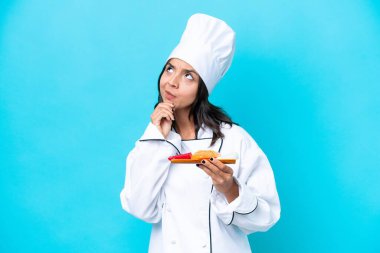 Genç İspanyol aşçı kadın elinde sashimi ile mavi arka planda izole edilmiş ve yukarı bakıyor.