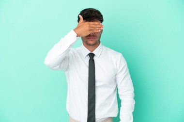 Kafkasyalı iş adamı mavi arka planda tek başına, gözleri elle kapatıyor. Bir şey görmek istemiyorum.