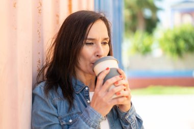 Orta yaşlı bir kadın elinde kahve tutuyor.