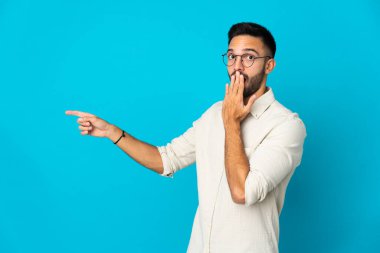 Young caucasian man isolated on blue background with surprise expression while pointing side