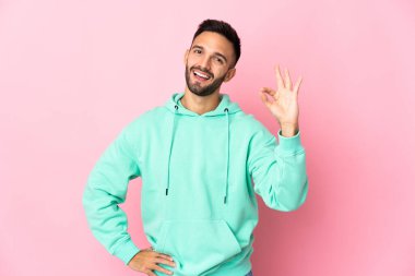 Pembe arka planda izole edilmiş genç beyaz adam parmaklarıyla tamam işareti gösteriyor.