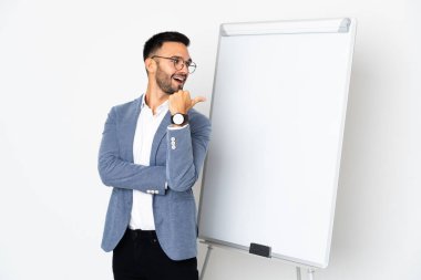 Beyaz arka planda izole edilmiş genç beyaz bir adam beyaz tahtada sunum yapıyor ve yan tarafı işaret ediyor.