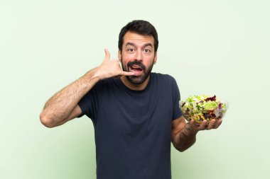 Yeşil duvarın üstünde salatalı genç yakışıklı bir adam telefon jesti yapıyor ve şüpheleniyor.