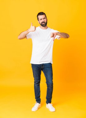 İzole edilmiş sarı arka planda sakallı bir adamın iyi-kötü bir işaret yaptığı uzun bir çekim. Evet ya da hayır arasında kararsız