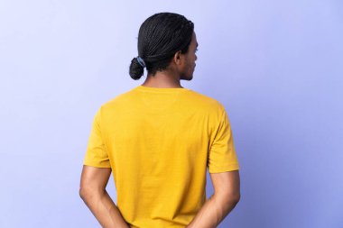 Örgülü genç Afrikalı Amerikalı adam mor arka planda izole edilmiş ve arkasına bakıyor.