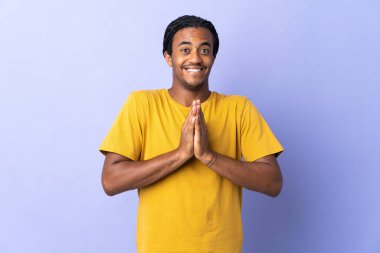 Mor arka planda izole edilmiş örgülü genç Afrikalı Amerikalı adam avuç içlerini bir arada tutuyor. İnsan bir şey ister.