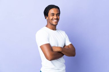 Örgülü genç Afrikalı Amerikalı adam mor arka planda izole edilmiş, kolları bağlı ve ileriye bakıyor.